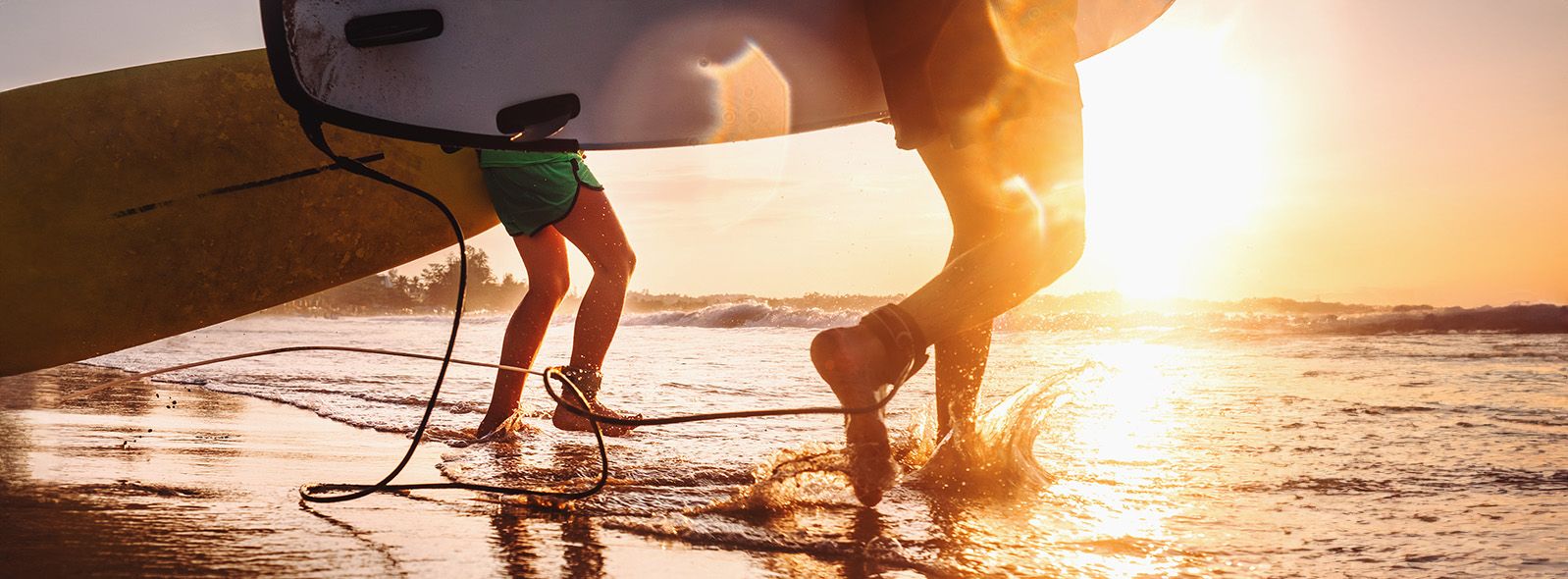 orangey sunset photo of father and son racing toward water carrying their surfboards.